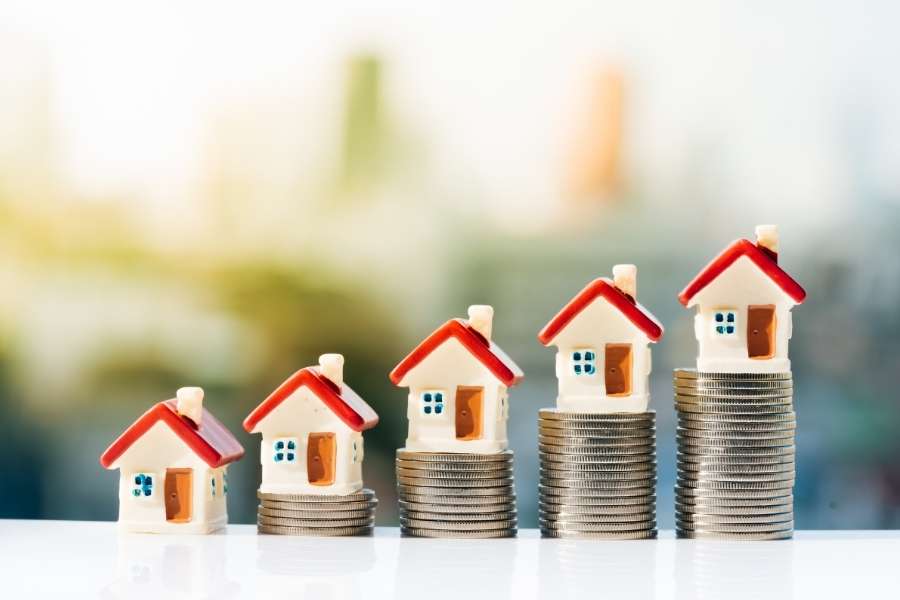 Plusieurs petites maquettes de maisons posées sur des piles de pièces de monnaie croissantes pour protéger son patrimoine immobilier.