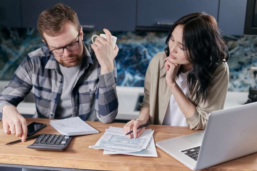 Un couple analyse des factures et utilise une calculatrice pour apprendre à mieux gérer son budget familial.